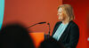 Bundesinnnenministerin Nancy Faeser lächelt an einem Rednerpult vor einem roten Hintergrund.